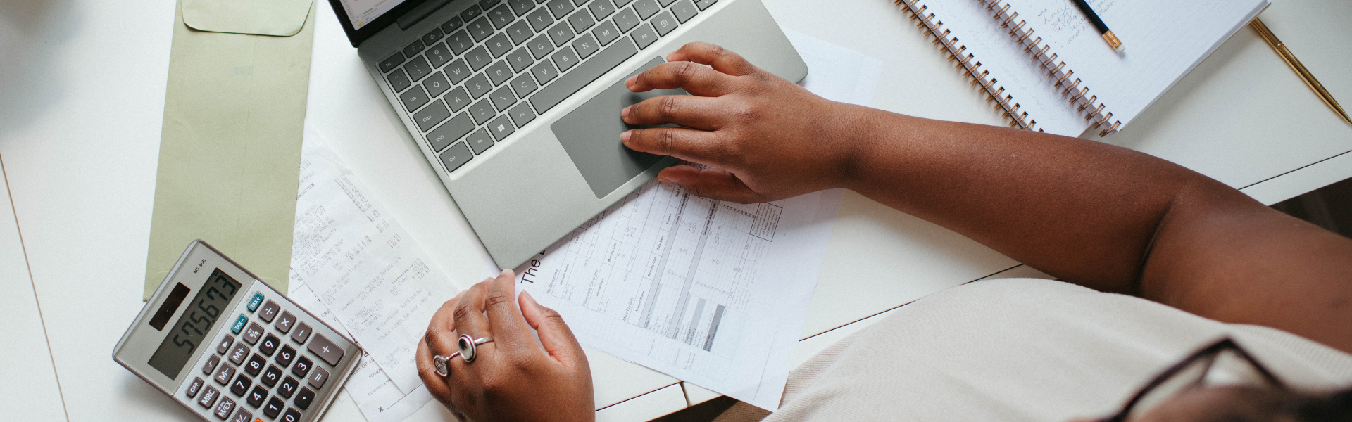 A photo of someone's hands at a computer working on budgeting and finances