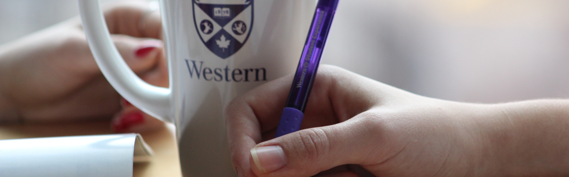 A close up of a hand writing on paper with a Western pen