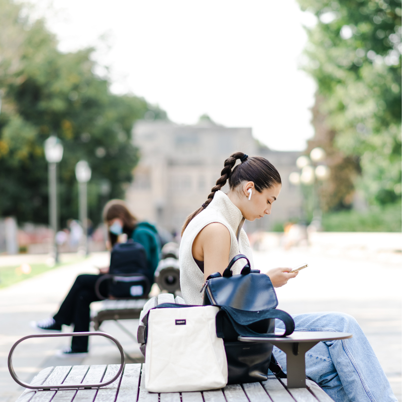 A student sitting at a outdoor table wearing headphonesor table wearing headphones looking at their phone