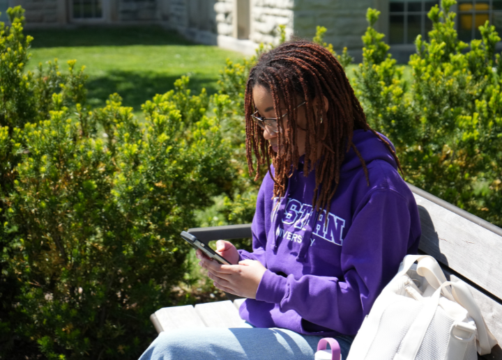 A student sitting on their phone outside on campus