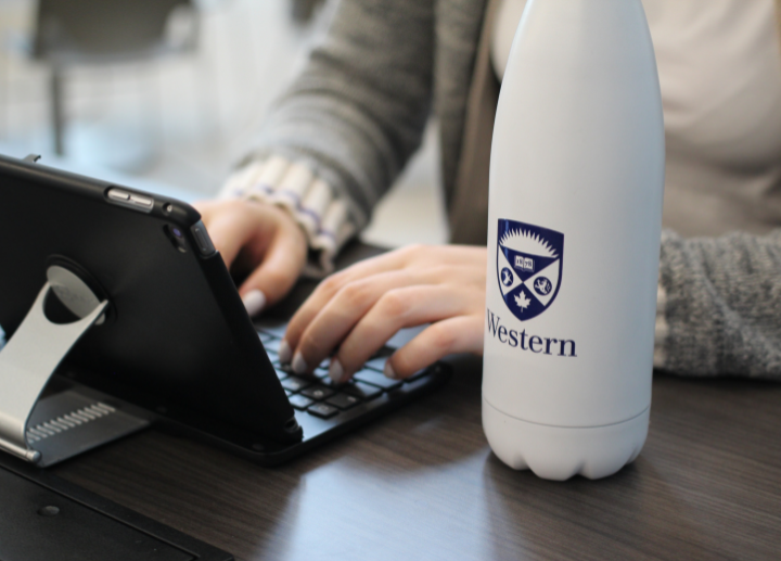 Person typing on a tablet with a Western University water bottle nearby