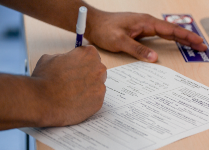 A hand holding a purple pen filing out a form